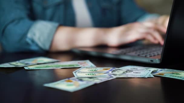 Honderd dollar biljetten vallen op tafel van freelancer werken op laptop — Stockvideo