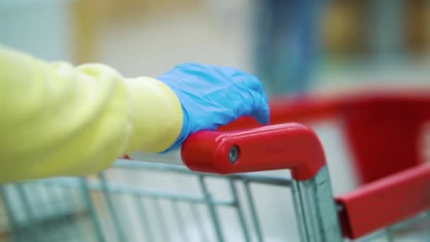 Tıbbi eldivenli kadın elleri süpermarkette alışveriş arabası itiyor. — Stok video