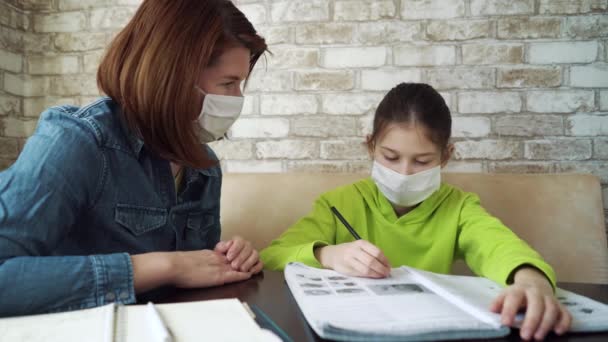 Madre e hija con máscaras médicas estudiando en casa durante la pandemia — Vídeos de Stock