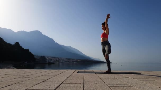 Όμορφο κορίτσι κάνει γιόγκα asanas δίπλα στη θάλασσα στην πρωινή λιακάδα — Αρχείο Βίντεο