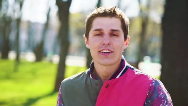 Joyeux jeune homme parlant à la caméra dans un parc ensoleillé — Video
