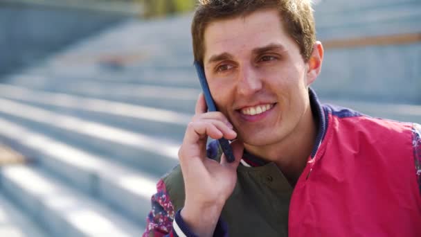 Portrait of young handsome man talking on phone on stairs outside — Stock Video