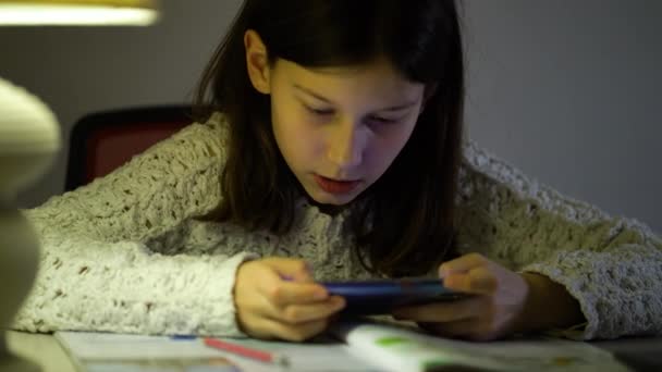 Возбужденная девушка играет в онлайн игры, используя смартфон дома в вечернее время — стоковое видео
