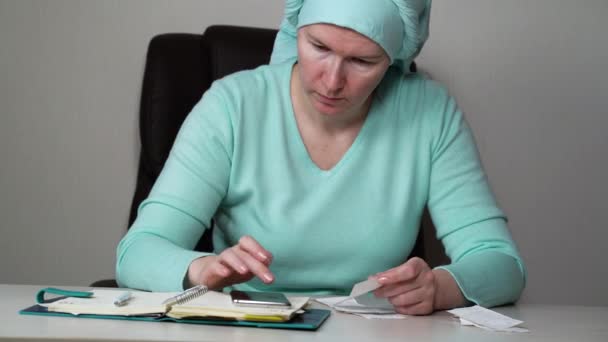 Kobieta w chustce sprawdza rachunki i zapisuje wydatki. — Wideo stockowe