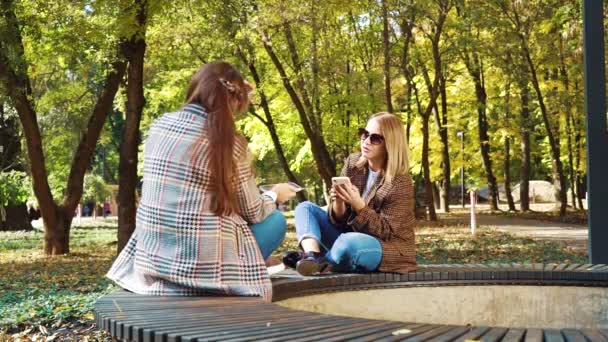 Hipster niñas navegando por las redes sociales utilizando teléfonos inteligentes en el hermoso jardín — Vídeo de stock