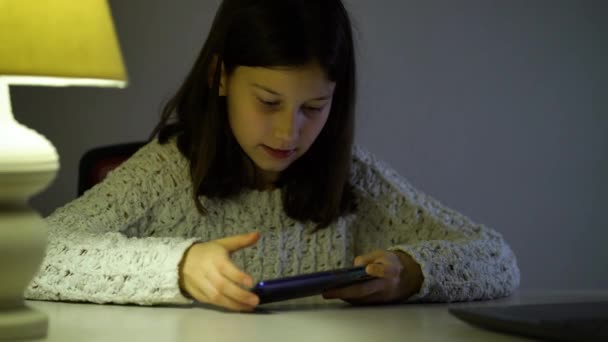 Pre-adolescente chica jugando juegos en línea en el teléfono inteligente en habitación oscura — Vídeo de stock