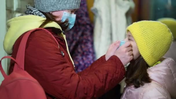 Заботливая мать надевает медицинскую маску на дочь перед выходом на улицу во время COVID — стоковое видео