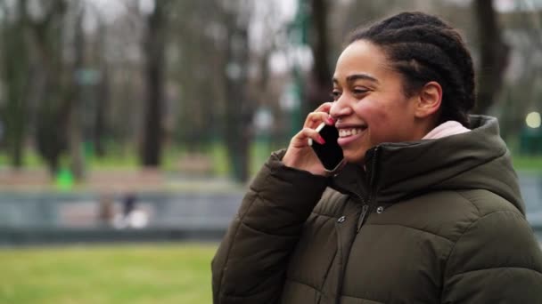 Cheerful black girl with afro braids talking on phone in park — Stock Video