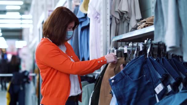 Mladá žena v lékařské masce nákup oblečení v supermarketu během pandemie — Stock video