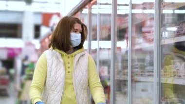 Maskeli kız süpermarkette buzdolabındaki ürünlere bakıyor.