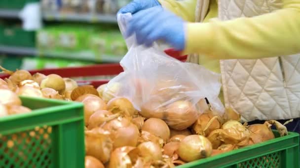 Crop vrouw in medische handschoenen zetten uien in plastic zak bij supermarkt — Stockvideo