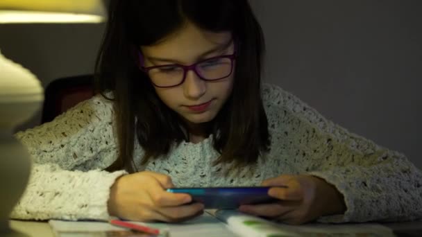 Chica emocional en gafas jugando juegos en el teléfono inteligente en la oscuridad — Vídeos de Stock