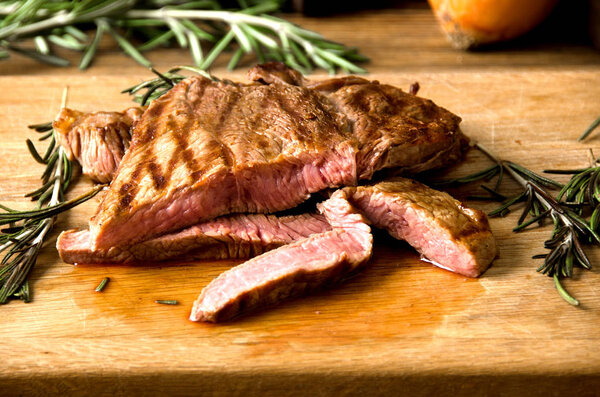 Rare steak rosemary rectangular wooden cutting board on a brown wooden background