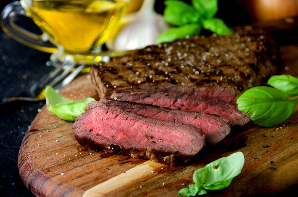 Sliced rare steak pepper salt cutting board on a dark background close up
