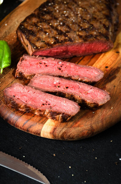 Chopped rare steak pepper salt cutting board on a dark background close up copy space