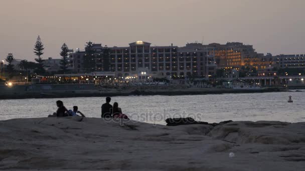 Ηλιοβασίλεμα σιλουέτα των νέων ζευγάρια συνεδρίαση ματιά στο παρασκήνιο στη θάλασσα και την πόλη. — Αρχείο Βίντεο