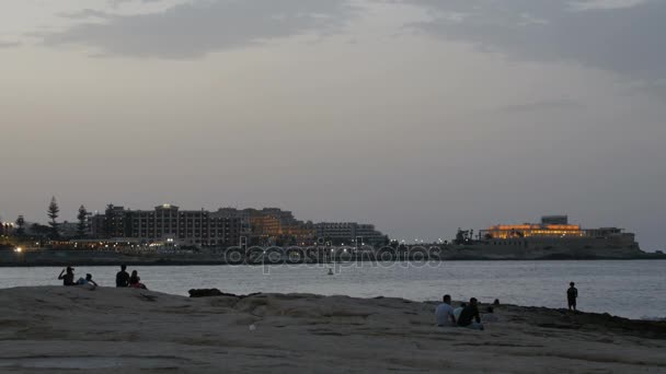 Ηλιοβασίλεμα σιλουέτα των νέων ζευγάρια συνεδρίαση ματιά στο παρασκήνιο στη θάλασσα και την πόλη. — Αρχείο Βίντεο