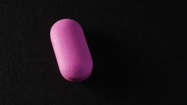 Сломанная розовая таблетка вращается на черной поверхности . — стоковое видео