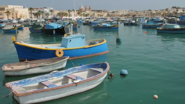 Marsaxlokk, Malta - 6 juli 2016: Prachtige visserij dorp architectuur met gekleurde boten op anker in een baai — Stockvideo