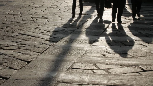 Silhouettes of people on the cobblestone pavement.