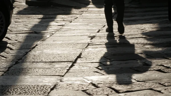 Silhouettes of people on the cobblestone pavement.