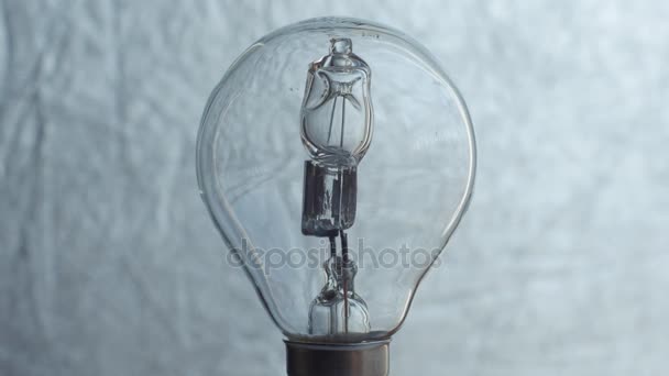 Närbild av glödlampa över silver bakgrund. Elektricitet. — Stockvideo