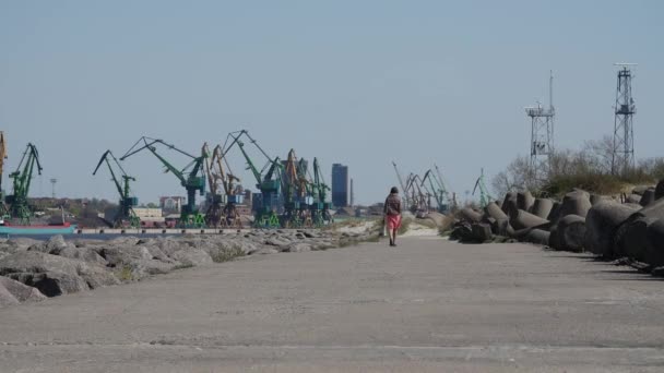 Unrecognizable people walking the rocks of jetty and breakwater to entrance of Klasipeda harbor, on hot summer day. — Stock Video