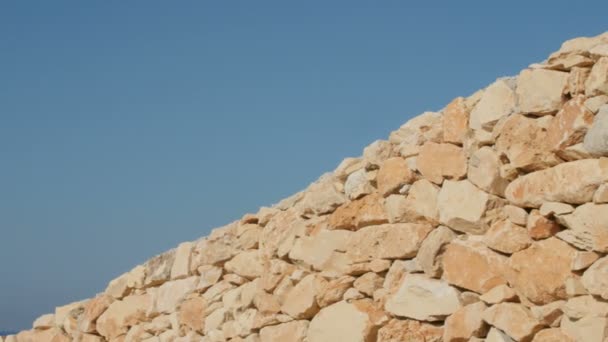 Um fragmento de uma parede de pedra amarela em um fundo azul céu — Vídeo de Stock