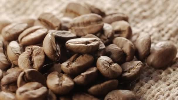Une poignée de grains de café bruns et torréfiés sur fond de toile de jute, gros plan, rotation — Video