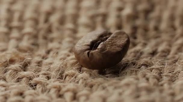 Un grano de café gira sobre un fondo de saco . — Vídeo de stock