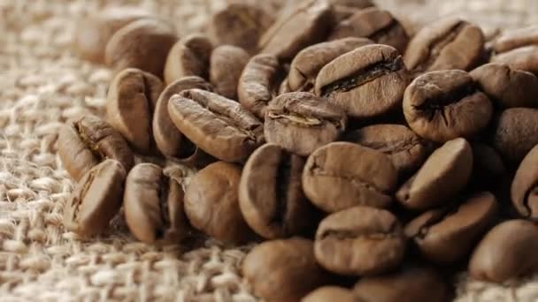 Жменька коричневих, смажених кавових зерен на мішковині тла, крупним планом, обертання — стокове відео