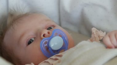 Üç aylık bebek battaniye var bir emzik ile yalan. Bebek yüz yakın çekim.