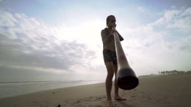 Genç müzisyen gün batımında didgeridoo plajında çalıyor..