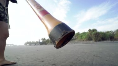 Genç müzisyen gün batımında didgeridoo plajında çalıyor..