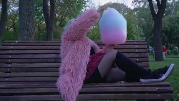 Playful girl tasting colorful cotton candy on bench, having fun in city park — Stock Video