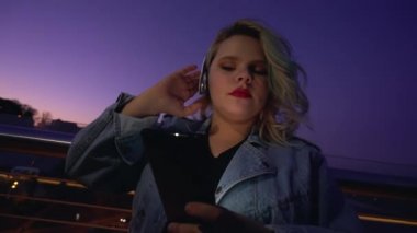 Kulaklıkla müzik dinleyen şehir kızı, geceleri multimedya uygulaması kullanıyor.