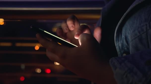 Primer plano de las manos de los adolescentes utilizando el teléfono inteligente en la ciudad nocturna, tecnología moderna — Vídeo de stock