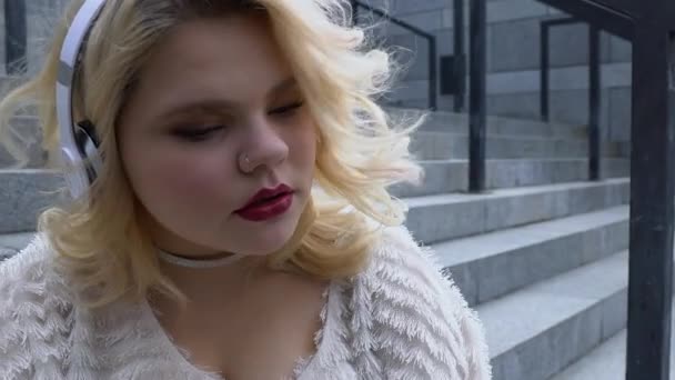 Pensive mooi meisje genieten van muziek in hoofdtelefoon, geïnspireerd door favoriete lied — Stockvideo