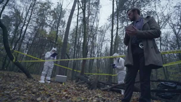 Kriminaltekniska experter samlar in bevis, skogsbrottsplats märkt med gul tejp — Stockvideo