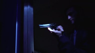 Dikkatli polis tabancayla karanlık odaya giriyor, suçluların yuvasını inceliyor.