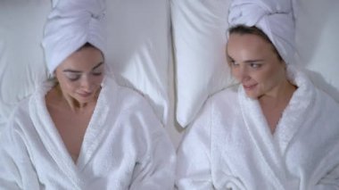 Neşeli kızlar havluya sarılı saçlarıyla yatakta uzanıp spa efektlerinin keyfini çıkarıyorlar.