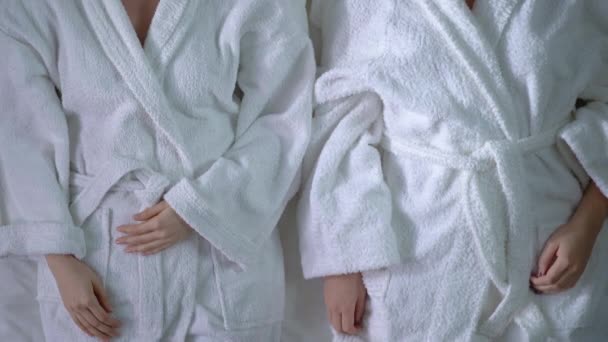 Дві молоді жінки лежать на ліжку в халатах, розслаблених після процедур догляду за красою — стокове відео