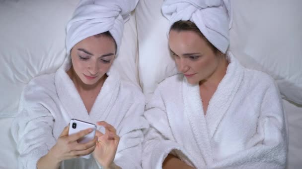 Flirty żeńskich przyjaciół w szlafrokach za pomocą aplikacji randkowej na gadżet, social media — Wideo stockowe