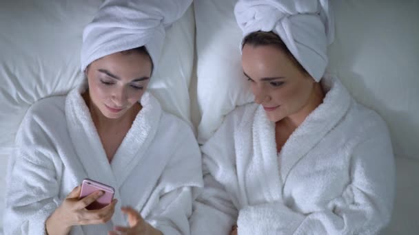 Девушки веселятся на пижамной вечеринке, просматривают интернет на смартфоне и смеются — стоковое видео