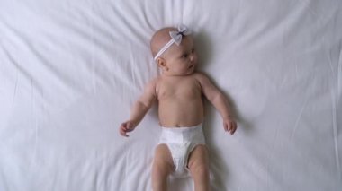 Aktif, yumuşak bebek bezi takan, yatağa uzanmış, hareket eden bacakları olan kız.