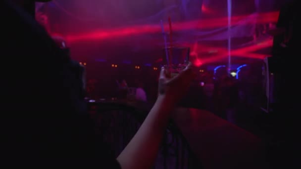 Молодая женщина тусуется в ночном клубе, бокал в руке, толпа на танцполе — стоковое видео