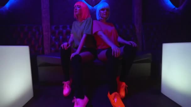 Флиртующие девушки сидят на диване ночного клуба, позируют соблазнительно для камеры, веселятся — стоковое видео