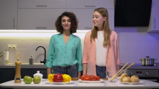 Dos jóvenes amigos sonriendo en cam, mirándose, cocinando en la cocina — Vídeo de stock