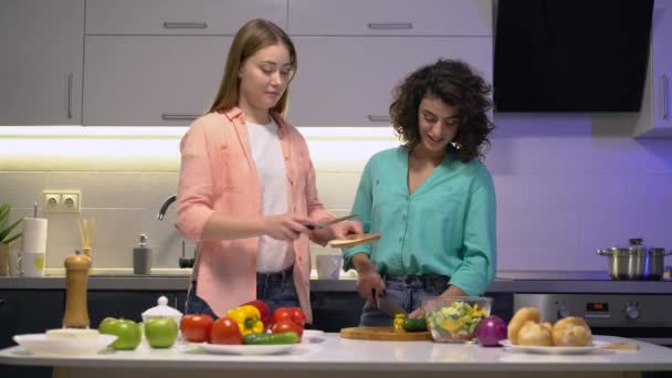 Hvit kvinne som klemmer en venninne, romkamerater som lager mat sammen hjemme – stockvideo