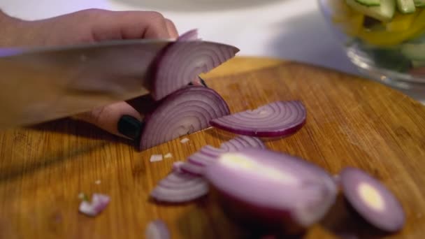 Домохозяйка режет красный лук на кухне, кладет салат ингредиенты в стеклянную миску — стоковое видео